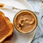 A jar of cinnamon butter on a white plate with two slices of toast and a knife beside it.