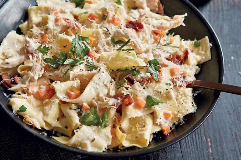 Creamy pappardelle with chicken and bacon in a black bowl with a fork, topped with grated cheese.
