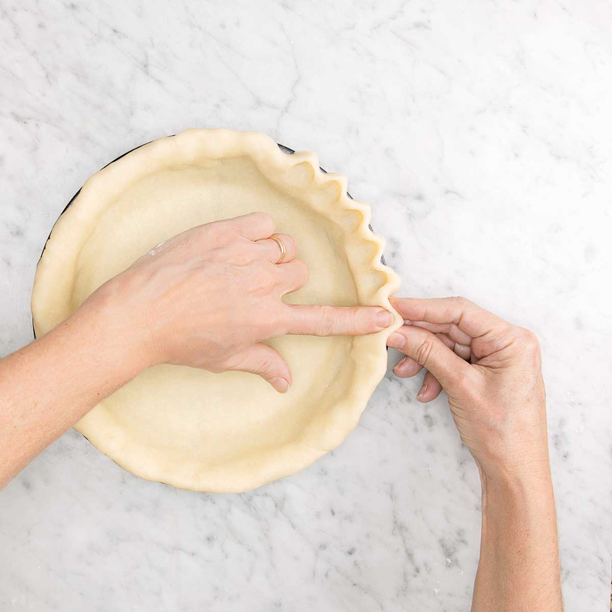 A person using their fingers to crimp a pie crust.