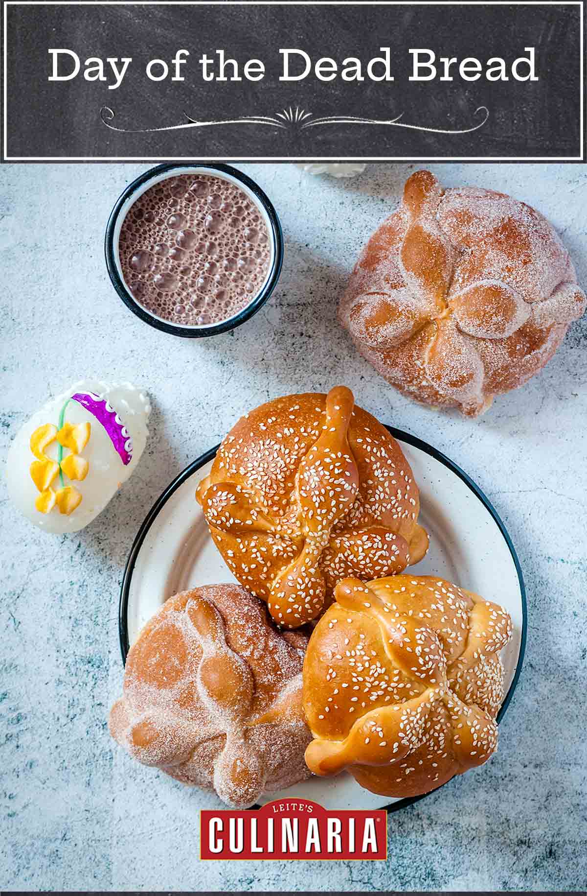 Day of the Dead bread on a plate, 2 with sugar and 2 with white sesame seeds, beside a cup of Mexican hot chocolate and a sugar skull.