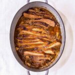 French onion brisket in an oval enamel casserole dish on a white background.