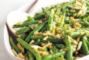 Green beans with browned butter and almonds in an oval white bowl with a serving spoon.