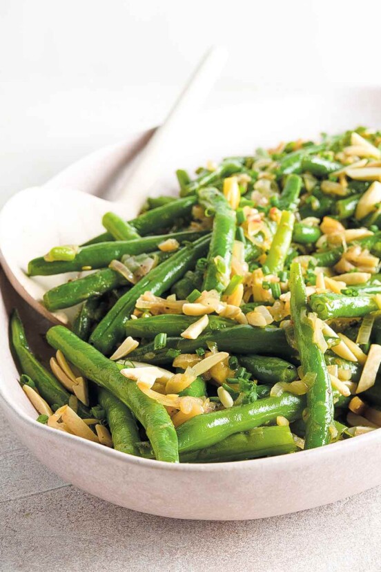 Green beans with browned butter and almonds in an oval white bowl with a serving spoon.