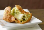 A hazelnut fresh herb popover, on a square white plate, split open with butter melting in the middle.