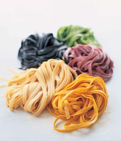 Homemade pasta dough in 5 colors, plain, squid ink, spinach, beet, and saffron on a white background.