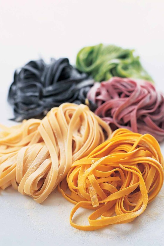 Homemade pasta dough in 5 colors, plain, squid ink, spinach, beet, and saffron on a white background.