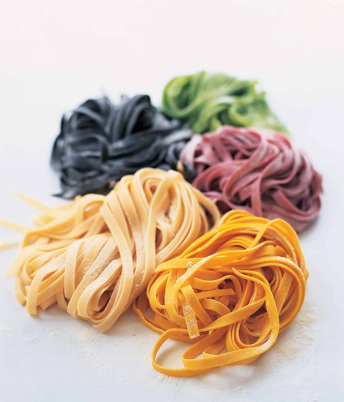 Hemlagad pastadeg i 5 färger, vanligt bläckfiskbläck, spenat, betor och saffran på vit bakgrund.