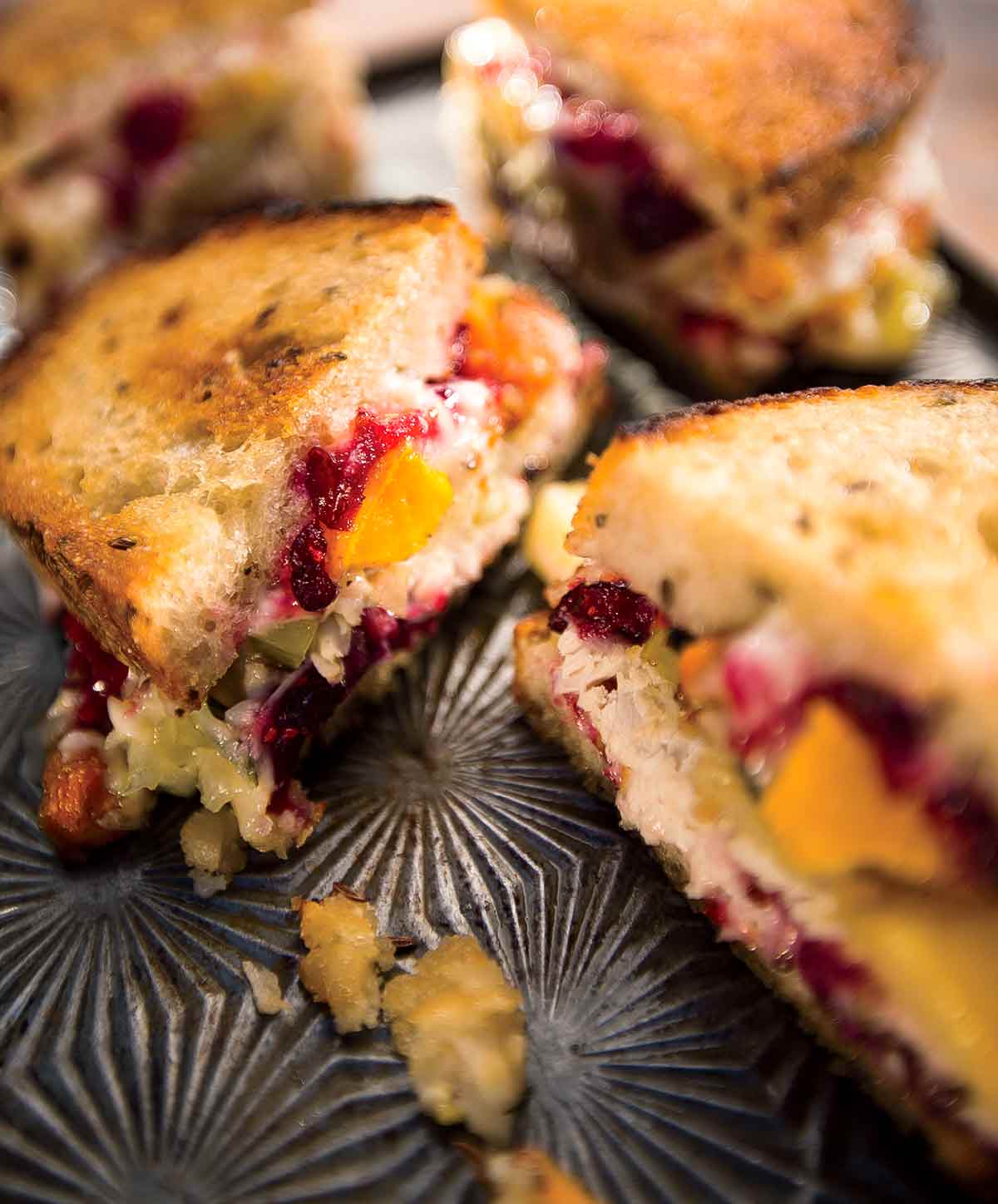 Two hot turkey sandwiches, sliced in half on a tray with pieces of cranberry, avocado, and stuffing lying beside them.