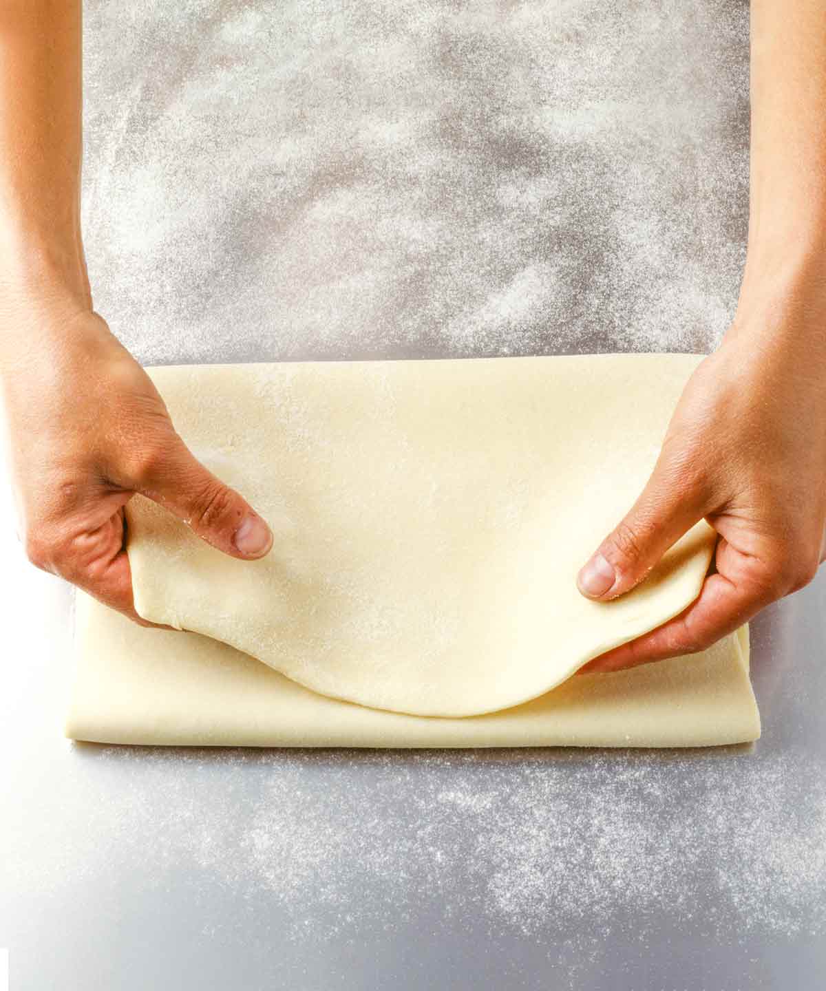 Extra flaky pie crust being folded in thirds from a large sheet of dough on a floured surface.