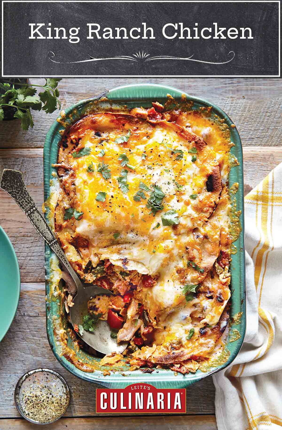 King Ranch chicken in a large green casserole dish with a serving spoon and a portion missing. A plate, a dish towel and a bowl of spices next to it.
