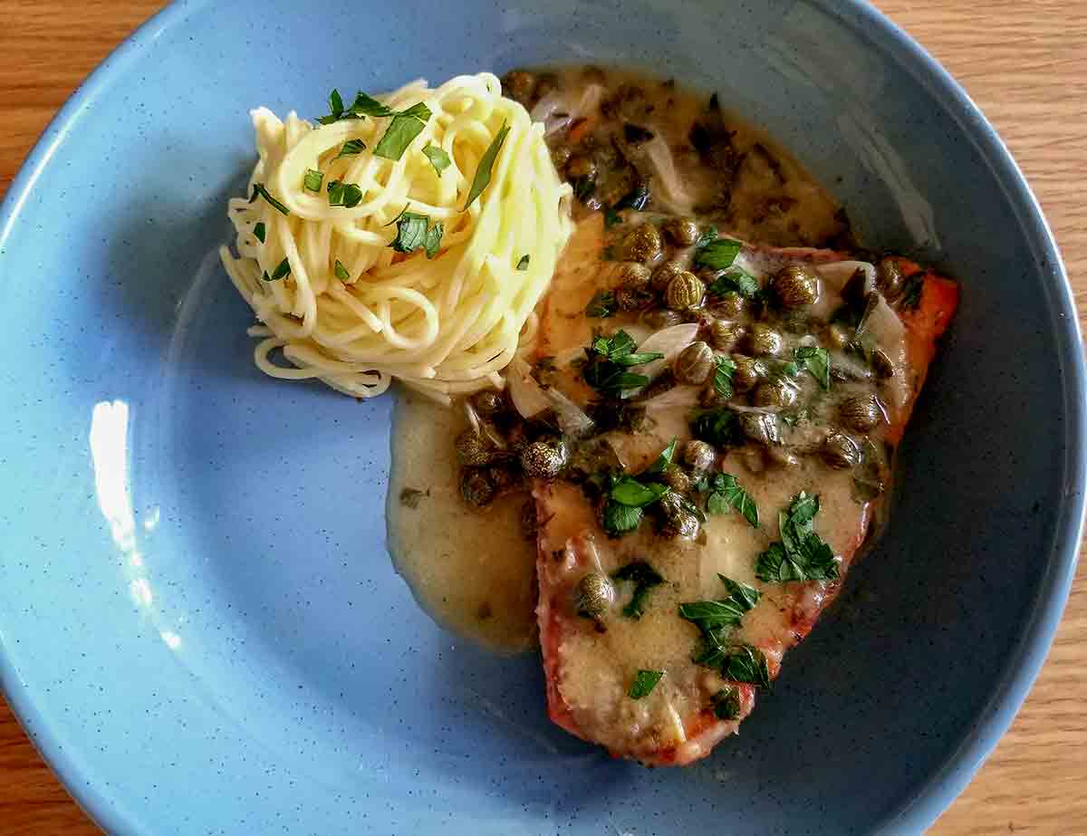 Lemon salmon piccata on a blue plate with a side of spaghetti noodles.