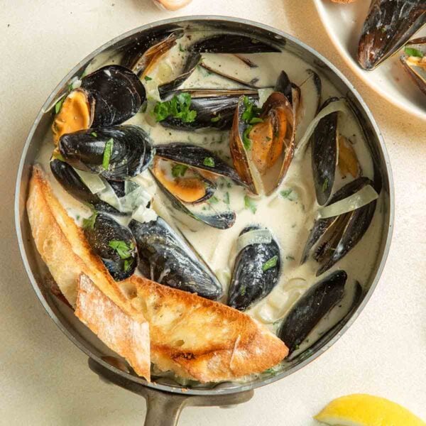 A copper saucepan filled with mussels in a creamy white wine garlic sauce with lemons.