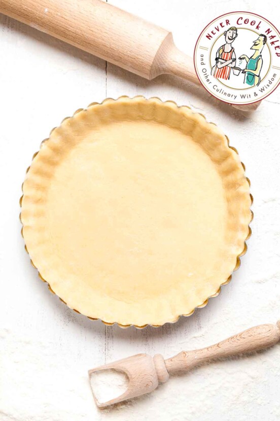 A pie crust in a fluted pie tine beside a flour scoop and a rolling pin.