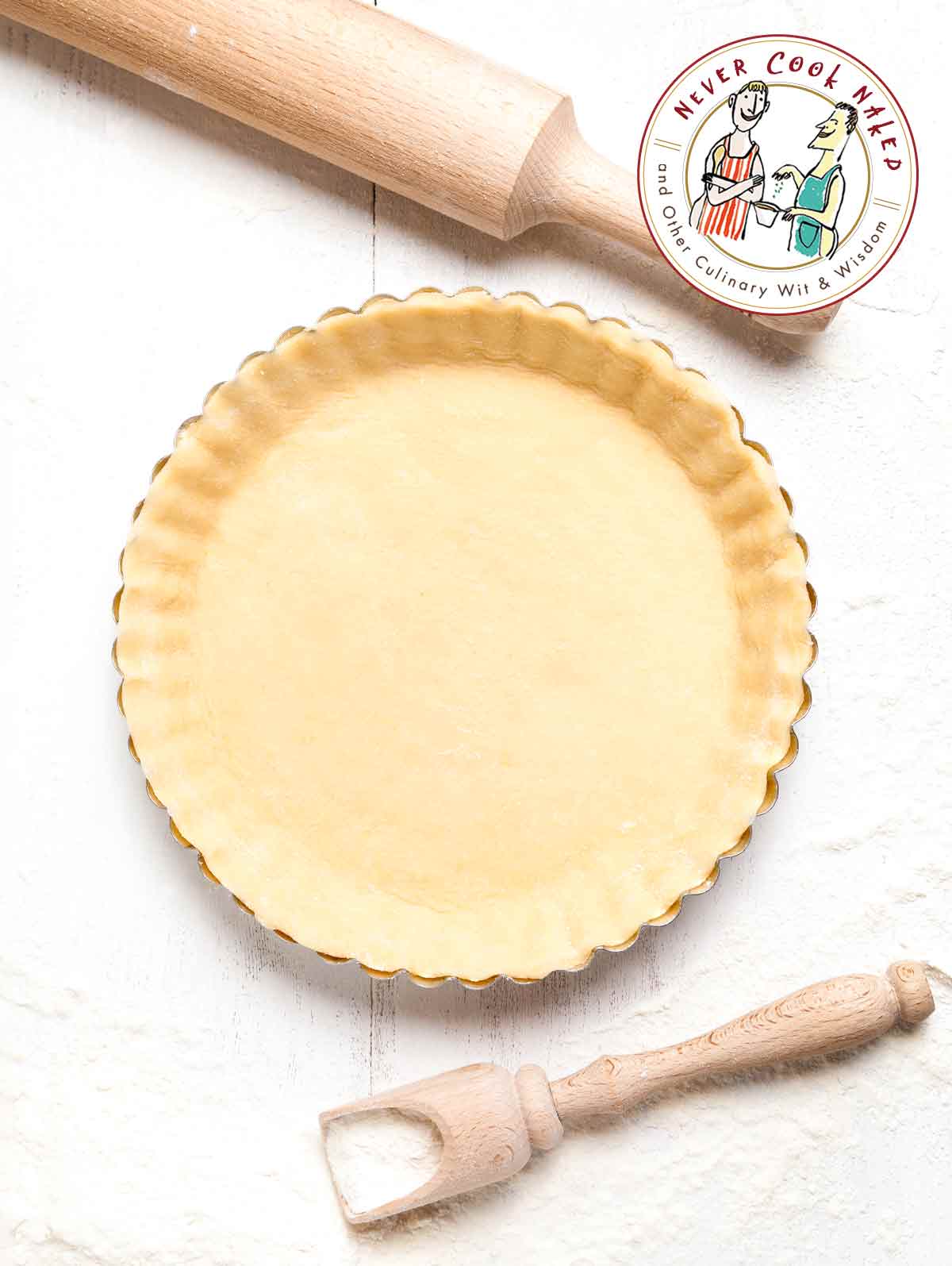 A pie crust in a fluted pie tine beside a flour scoop and a rolling pin.