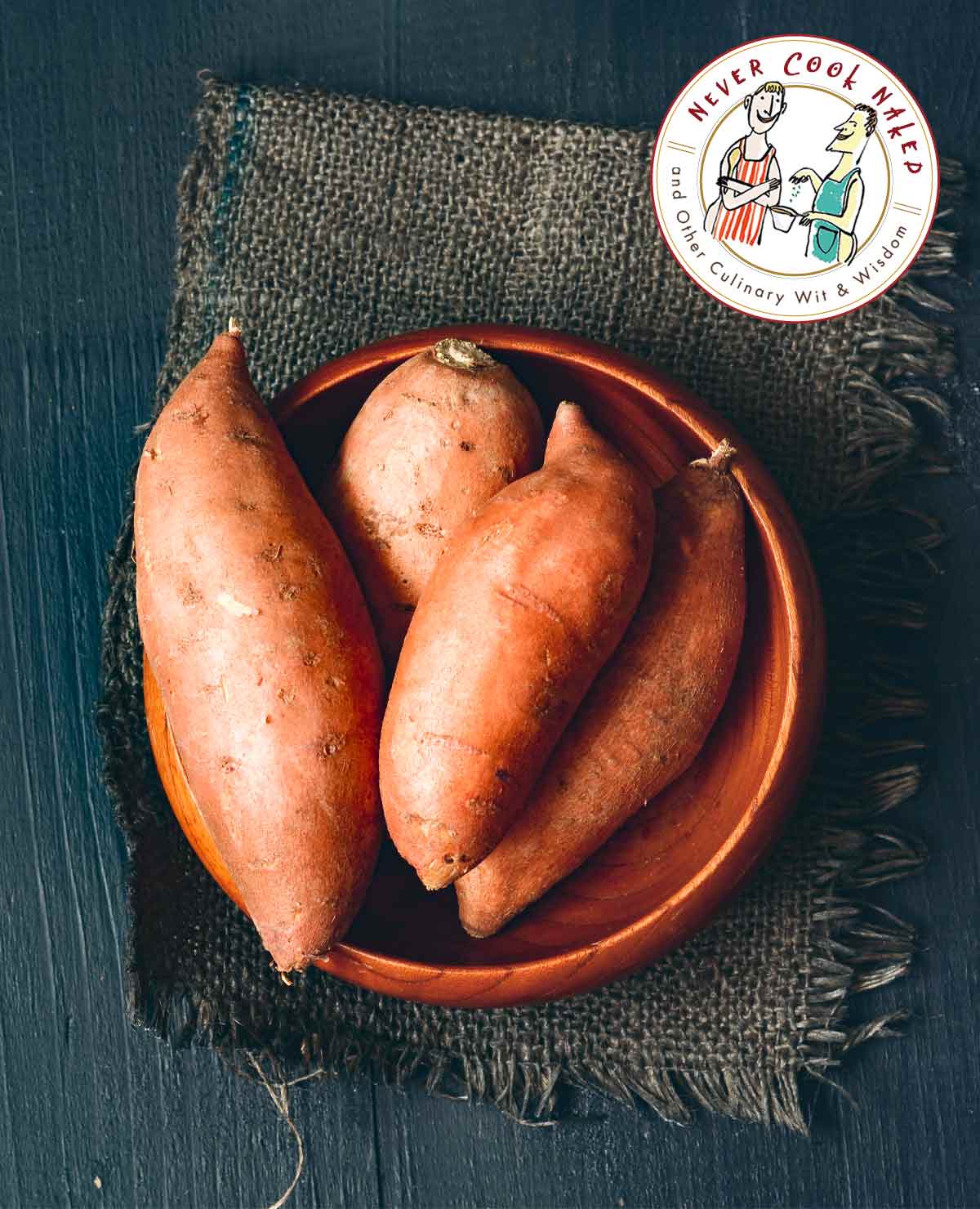 Four sweet potatoes in a wooden bowl on a piece of burlap.