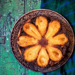 A pear and cardamom caramel upside-down cake on a carved wooden plate, on a green wooden table.