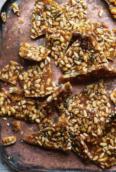 Pine nut brittle broken into irregular pieces on a large brown tray.