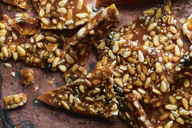 Pine nut brittle broken into irregular pieces on a large brown tray.