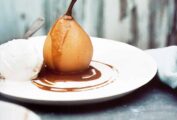 A poached pear with warm coffee sauce on a plate with a scoop of vanilla ice cream and a spoon.