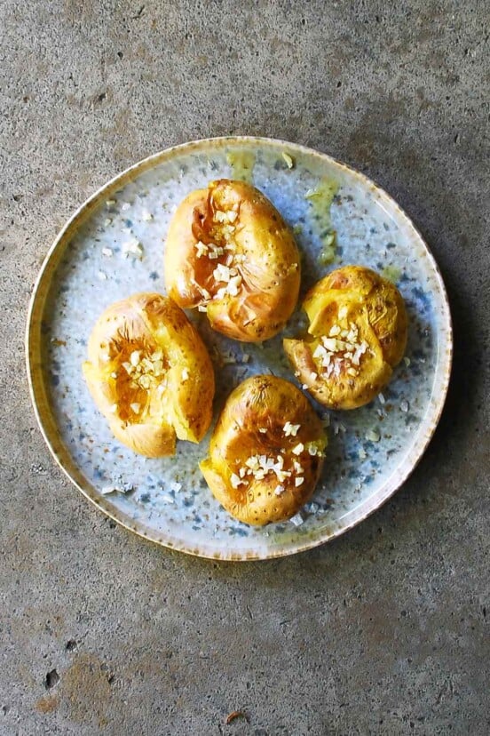 Portuguese smashed potatoes covered with minced garlic, olive oil, and salt, on a blue pottery plate.