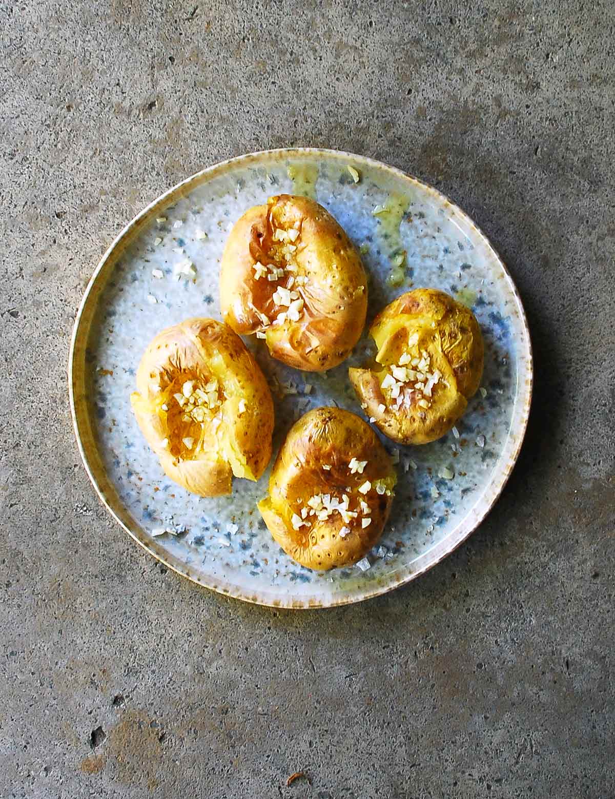 Portuguese smashed potatoes covered with minced garlic, olive oil, and salt, on a blue pottery plate.