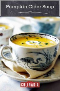 Pumpkin cider soup in a blue and white teacup, garnished with crème frâiche and chives.