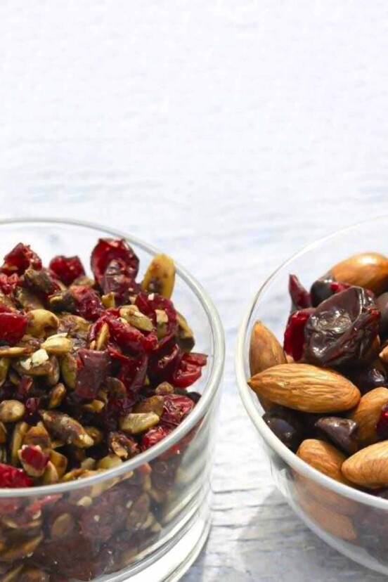 Pumpkin crunch in a glass bowl beside a glass bowl of mixed nuts and cranberries.