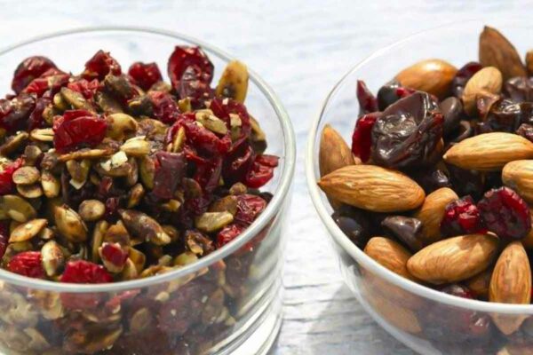 Pumpkin crunch in a glass bowl beside a glass bowl of mixed nuts and cranberries.