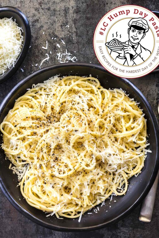 Quick cacio e pepe in a large black serving bowl beside a bowl of shredded cheese and a bowl of black pepper.