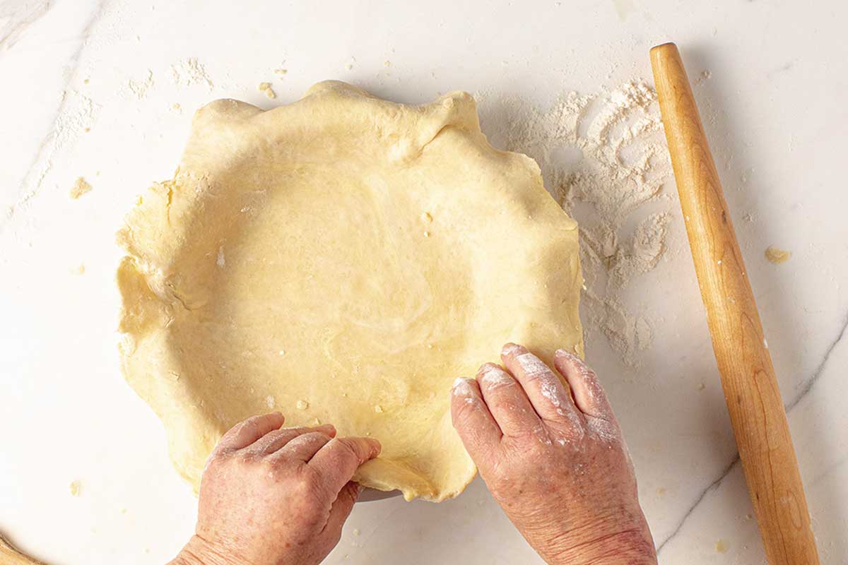 A person arranging a rolled out pie crust in a pie plate.