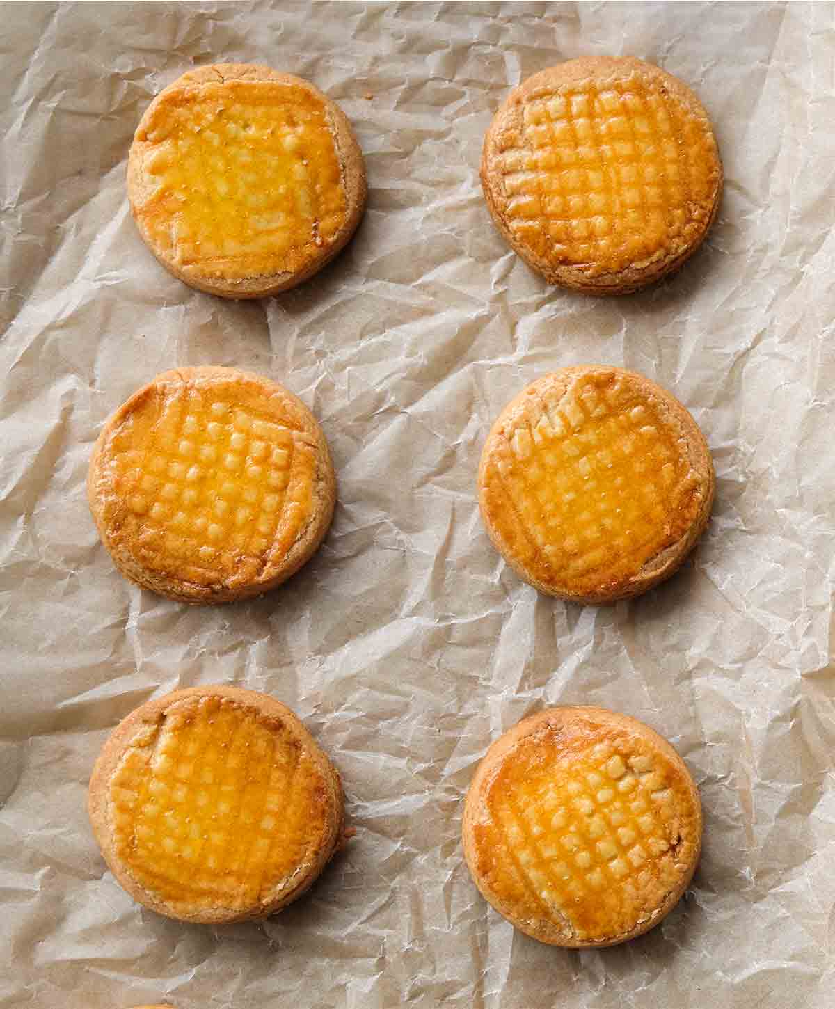 Sablés Breton with crosshatched tops, in two rows, on a crinkled sheet of parchment paper.