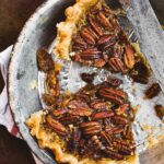 Spiced maple pecan pie, with only two pieces remaining, in a metal pie plate on a kitchen towel.