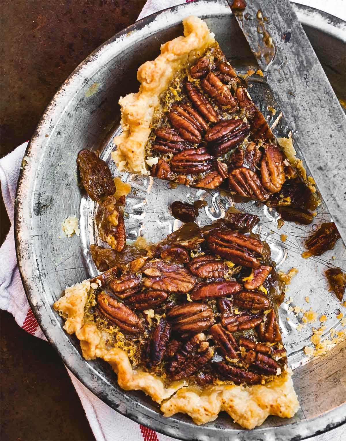Two slices of spiced maple pecan pie in a metal pie plate on a kitchen towel.