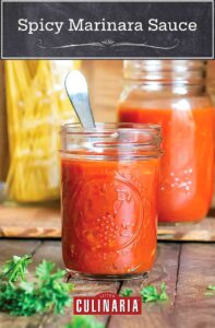 Spicy marinara sauce in a small mason jar with a spoon, with a larger mason jar, a jar of dry spaghetti, and parsley in the background.