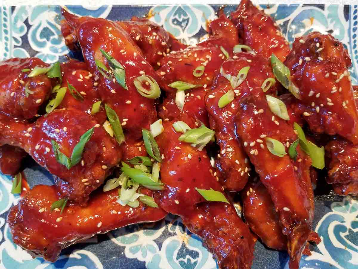 Sweet and spicy chicken wings, garnished with green onions and sesame seeds on a blue and white plate.