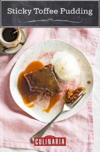 Sticky toffee pudding with vanilla ice cream on a white plate with a fork, beside a small bowl of extra toffee sauce.