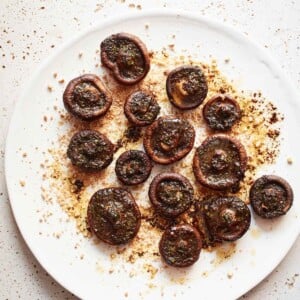 Stuffed mushrooms with chives and black pepper on a white plate, garnished with chopped cashews.