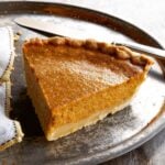 A slice of sweet potato pie on a large metal plate with a napkin and a knife.