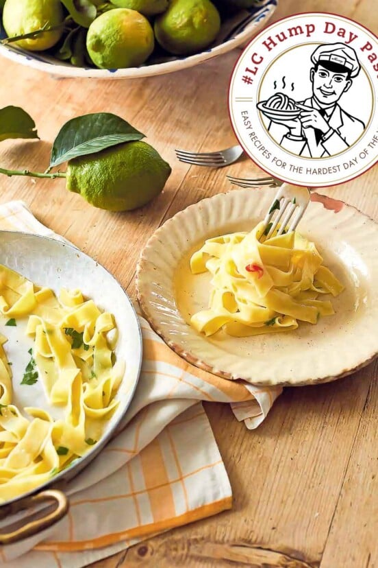 Tagliatelle with lemon on a large serving pate beside a smaller plate with noodles being twirled on a fork. Next to it, there are more forks and some lemons.