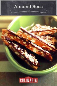 Almond roca in a green bowl, broken layers of chocolate, caramel, and sliced almonds, on striped fabric