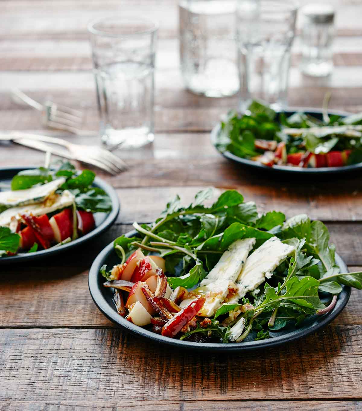 Arugula, pear, and blue cheese salad on three plates, beside glasses of water, forks, and a salt shaker.