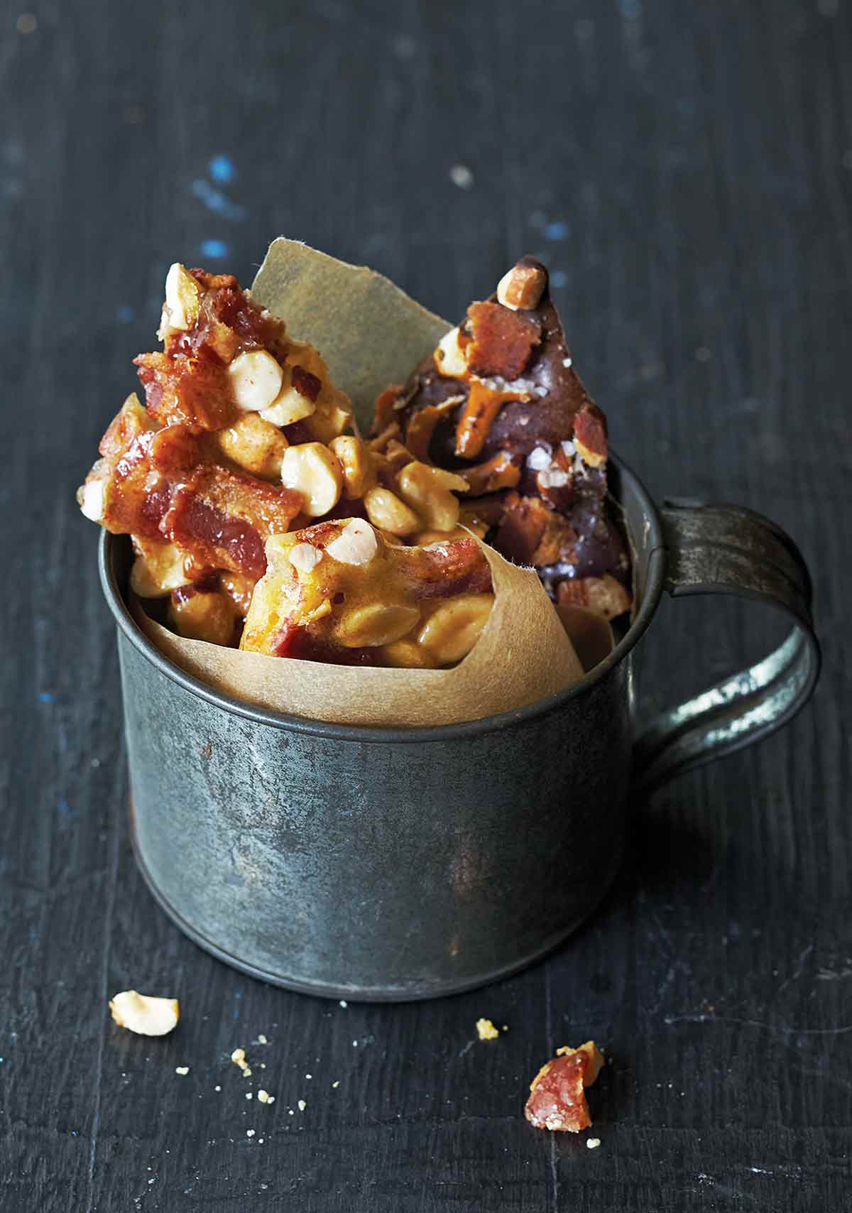 Bacon peanut brittle in shards, in a mug lined with parchment paper.