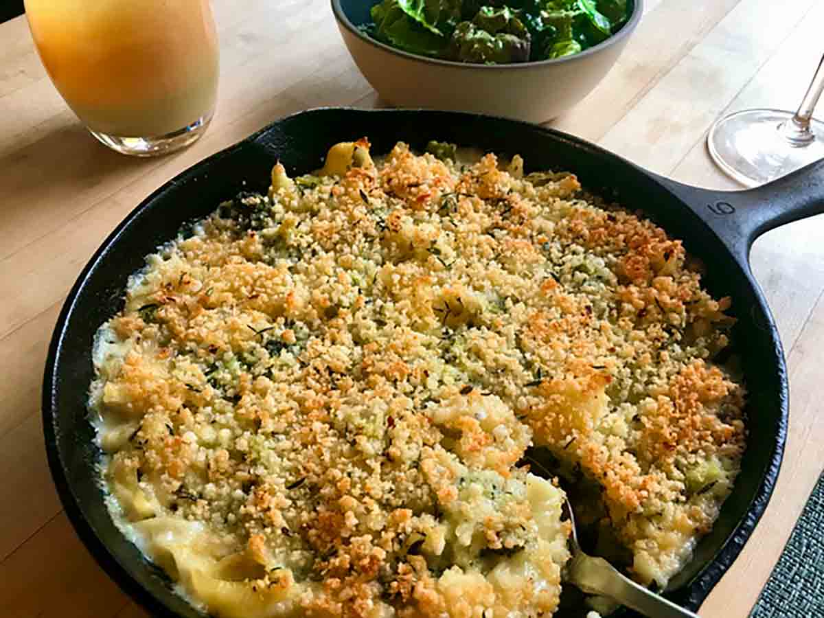 A cast-iron skillet filled with baked cheesy pasta with broccoli.