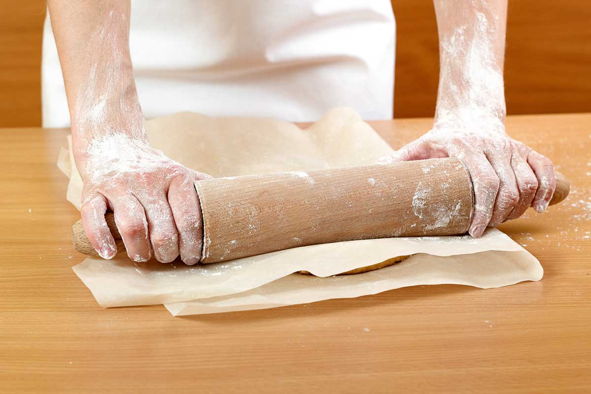 A person rolling out dough between sheets of parchment paper, one of our best tips for baking.