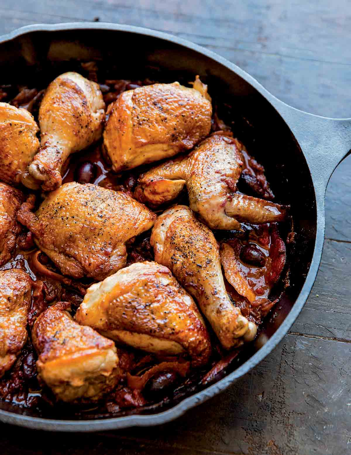 Braised chicken with olives and orange in a cast-iron skillet on a wooden table.