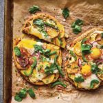 Two breakfast naan pizzas on a baking sheet covered with parchment paper and garnished with cilantro.
