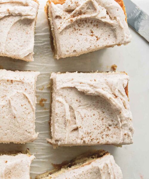 Brown butter snickerdoodle cake cut into six pieces on a piece of parchment paper, with a serving knife nearby.