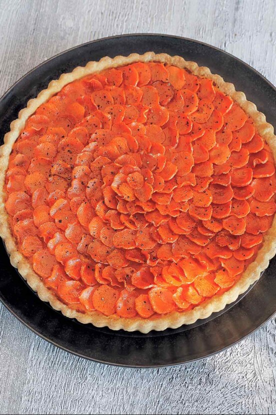 Carrot crostata on a large black plate, with a white napkin on a wood table.