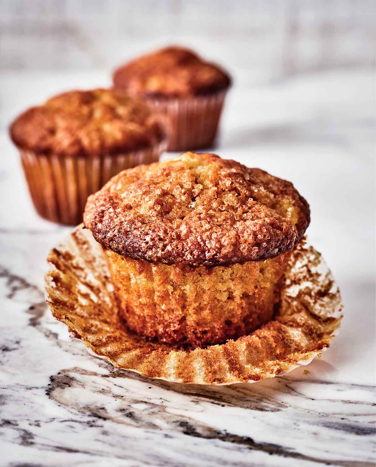 Carrot, pineapple, and candied ginger muffins on a counter, the one in front has its liner peeled off.