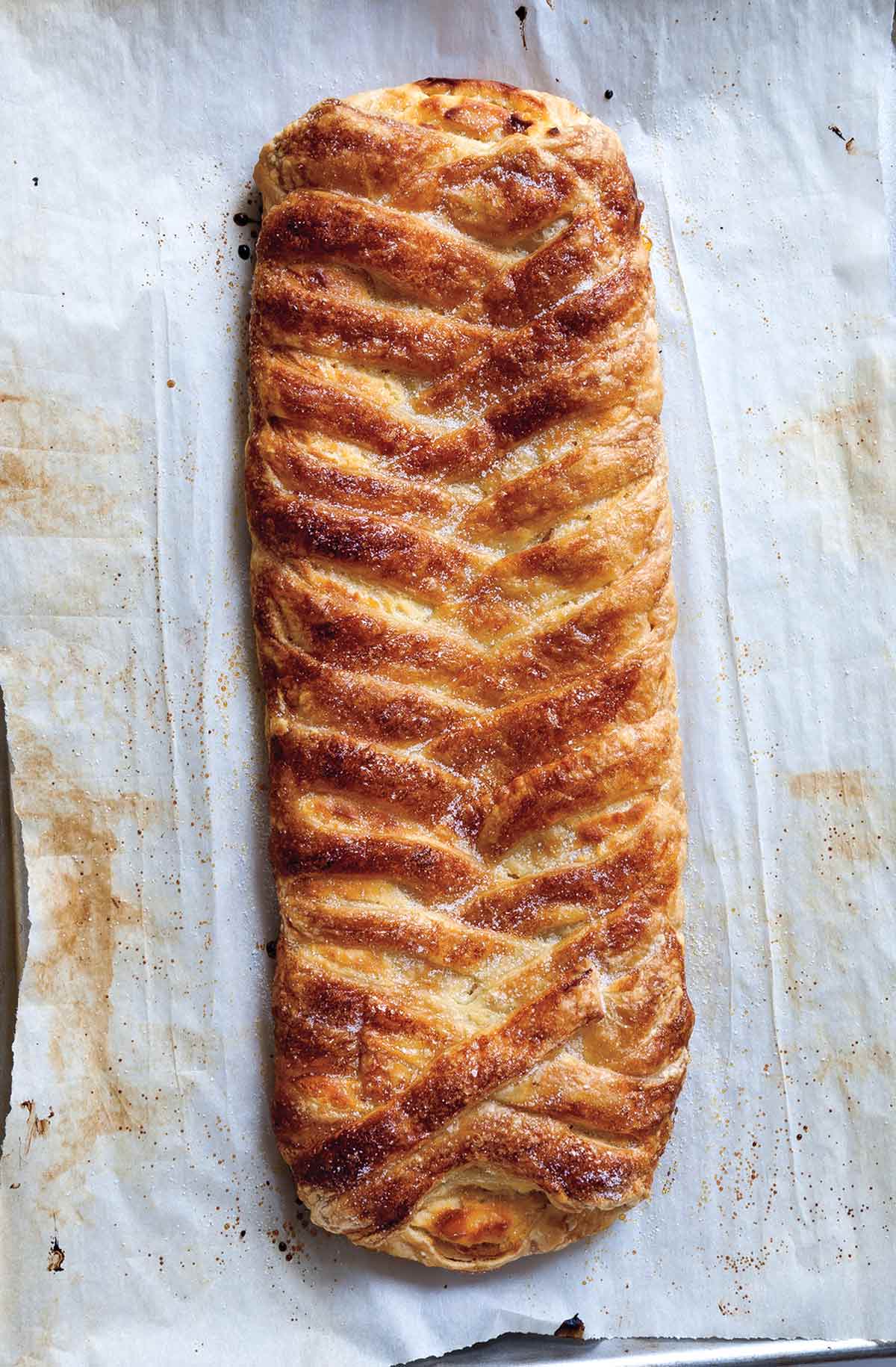 Cheese danish braided and sprinkled with sugar, on a sheet of parchment paper.